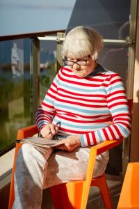 Personne âgée faisant des mots mêlés à gros caractères sur une feuille imprimée, assise à une table avec un stylo.